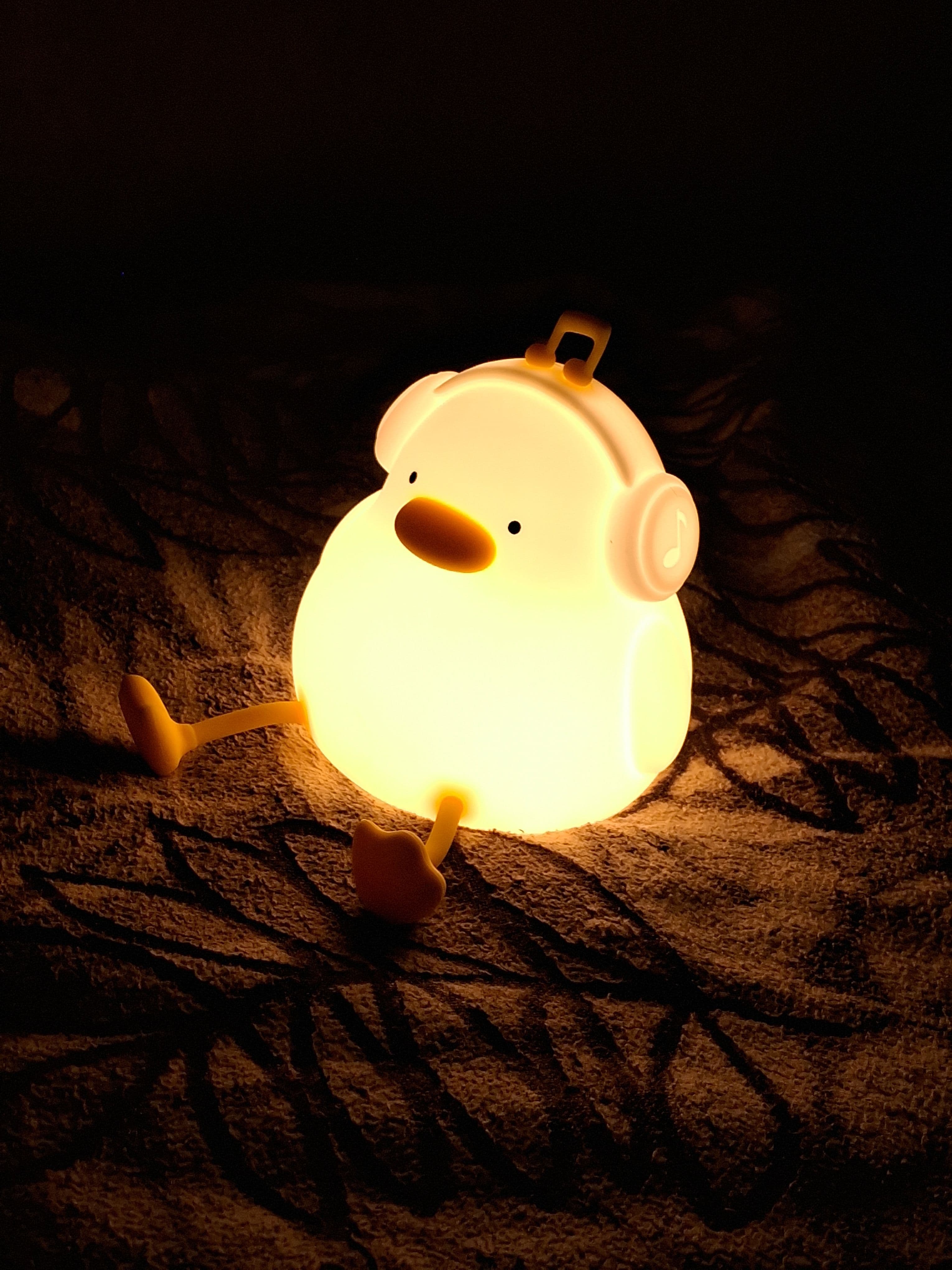 Duck-shaped night light glowing warmly on a blanket in a dark room