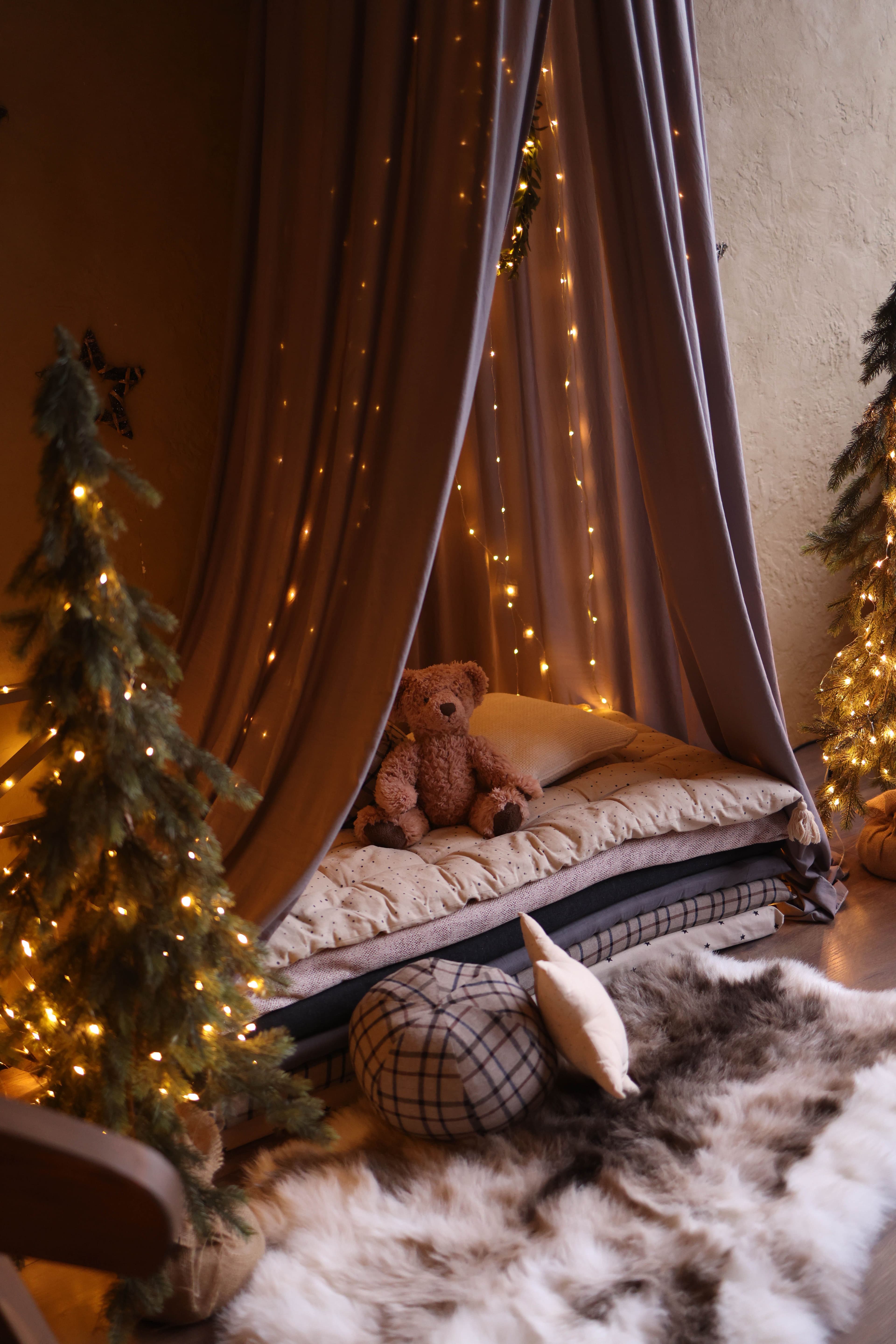 A string of warm fairy lights hung around a cosy reading nook with a stuffed bear and a plush toy